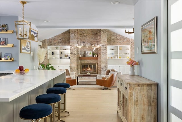 4704 Wild Briar Pass, Austin, TX 78746 - kitchen featuring a chandelier, brick wall, light wood-style flooring, a breakfast bar, and a fireplace
