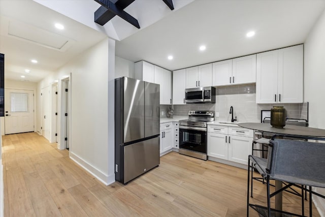 kitchen with stainless steel appliances, white cabinets, light countertops, decorative backsplash, and light wood finished floors