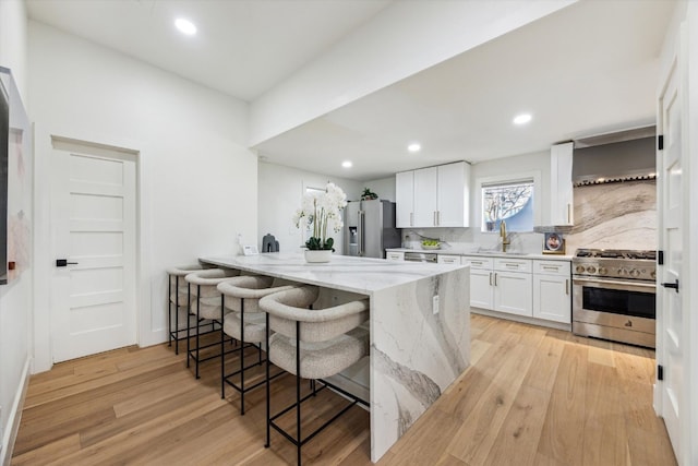 kitchen featuring light stone counters, stainless steel appliances, a breakfast bar, white cabinets, and wall chimney range hood