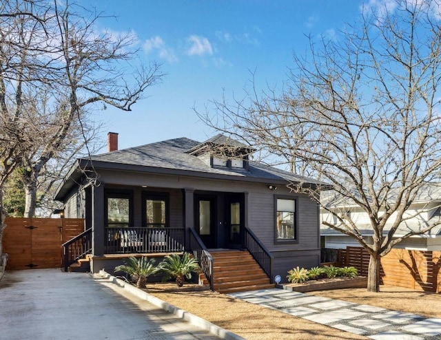 bungalow with covered porch, a shingled roof, and fence