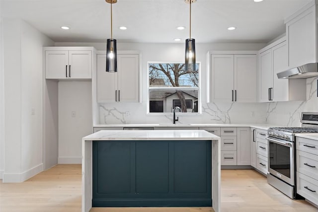 kitchen with light wood finished floors, a kitchen island, a sink, under cabinet range hood, and stainless steel gas range oven