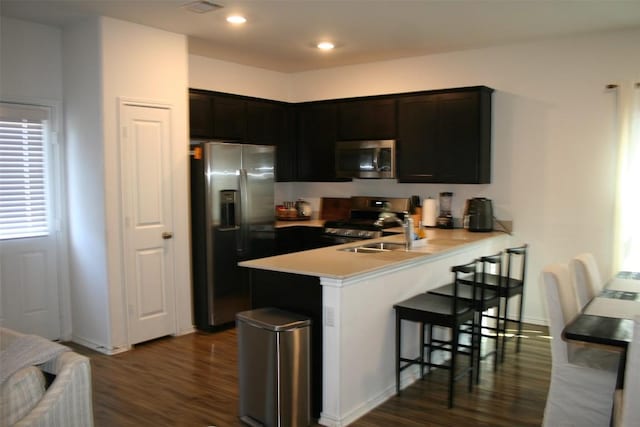 kitchen with stainless steel appliances, a peninsula, a sink, a kitchen breakfast bar, and light countertops