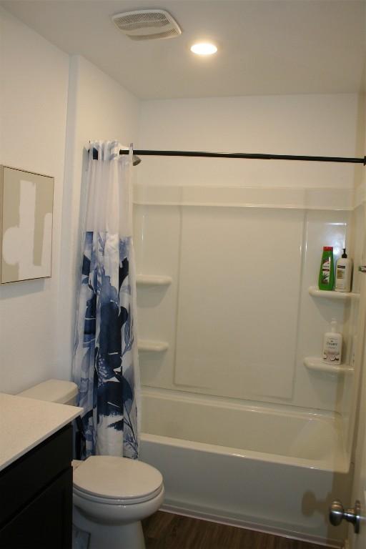 bathroom with toilet, wood finished floors, vanity, visible vents, and shower / bathtub combination with curtain