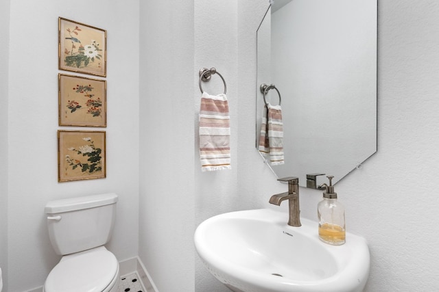 half bath featuring baseboards, a sink, and toilet