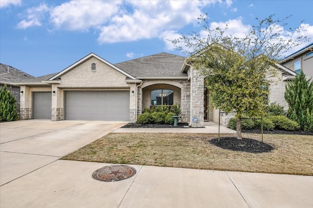 view of front of property featuring an attached garage, stone siding, concrete driveway, and roof with shingles