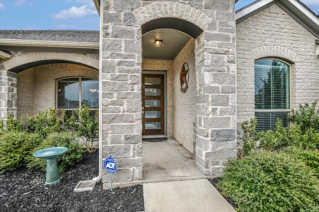 doorway to property with stone siding, brick siding, and roof with shingles