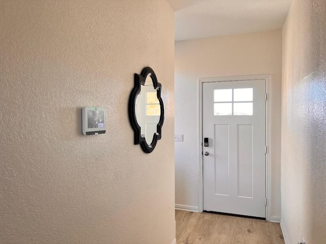 doorway featuring light wood-style flooring, baseboards, and a textured wall