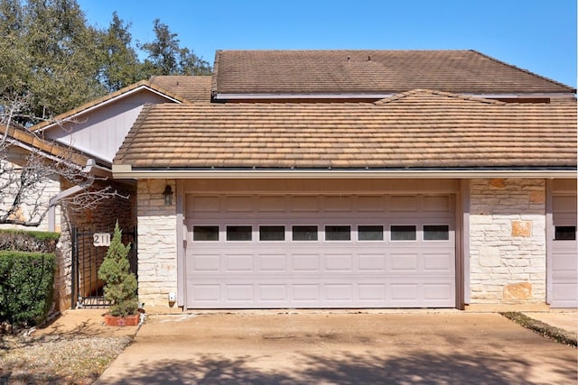 view of front of home with stone siding, a tiled roof, and concrete driveway