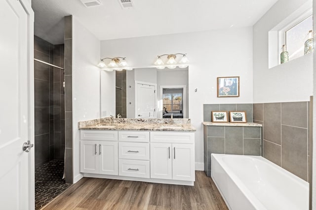 full bath with double vanity, visible vents, wood finished floors, a garden tub, and a tile shower