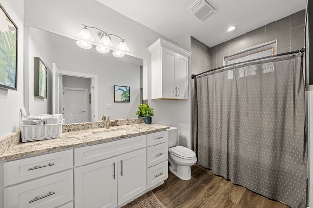 bathroom with toilet, a shower with shower curtain, wood finished floors, vanity, and visible vents