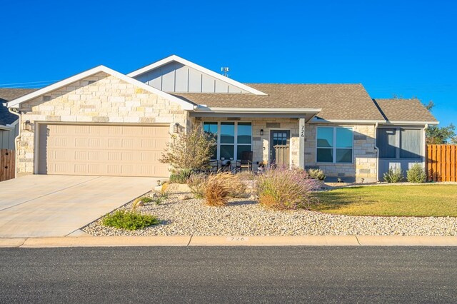 view of front of home featuring an attached garage, fence, stone siding, driveway, and board and batten siding