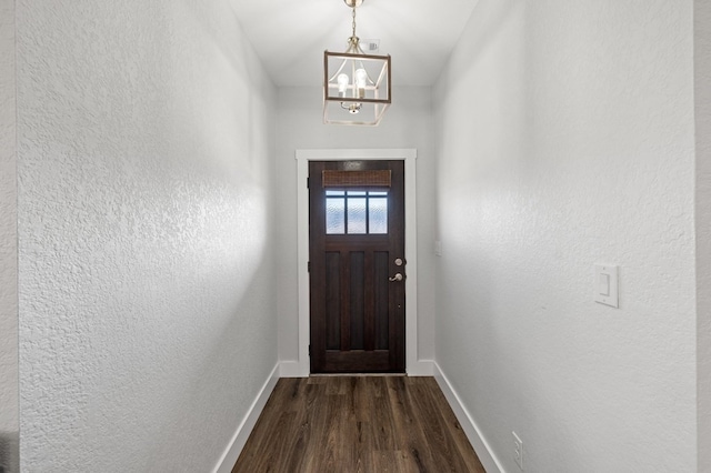 doorway to outside featuring dark wood-style floors, a textured wall, baseboards, and an inviting chandelier