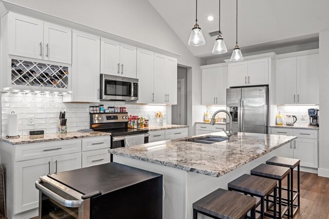 kitchen featuring lofted ceiling, stainless steel appliances, white cabinetry, an island with sink, and pendant lighting