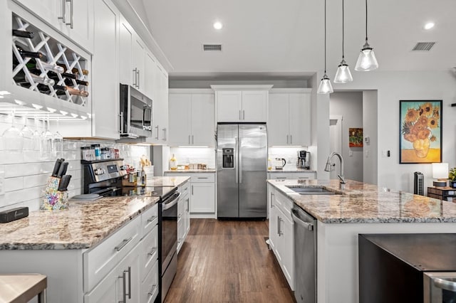 kitchen featuring a kitchen island with sink, stainless steel appliances, a sink, white cabinetry, and hanging light fixtures