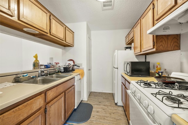 kitchen featuring visible vents, light countertops, a sink, white appliances, and under cabinet range hood