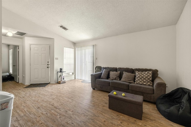 living area featuring lofted ceiling, light wood-style flooring, a textured ceiling, and visible vents