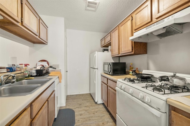 kitchen with white appliances, light wood-style floors, light countertops, under cabinet range hood, and a sink