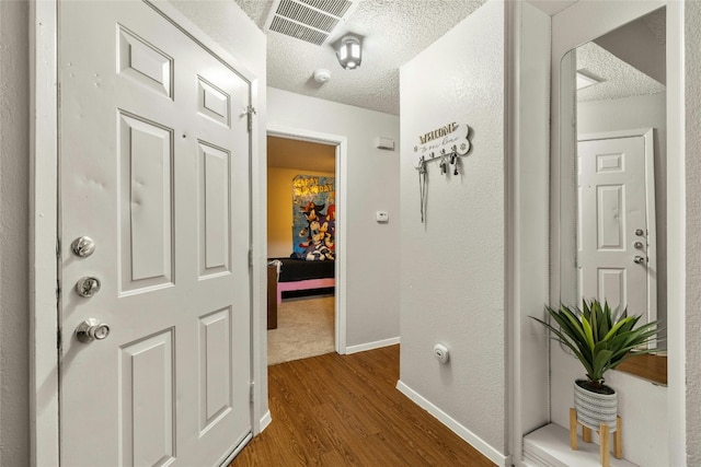 hall with baseboards, visible vents, dark wood-style flooring, and a textured ceiling