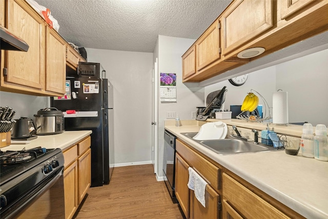 kitchen with light wood-style floors, wall chimney range hood, light countertops, black appliances, and a sink