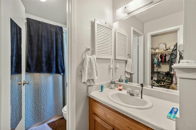 bathroom with a textured ceiling, toilet, a walk in closet, and vanity