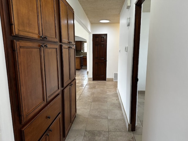 hallway featuring arched walkways, visible vents, and baseboards