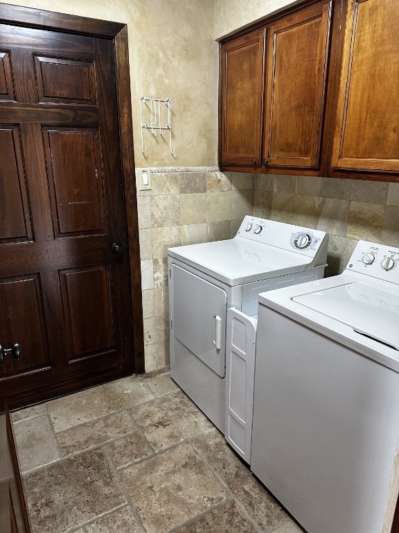 washroom featuring cabinet space, stone tile floors, tile walls, and independent washer and dryer