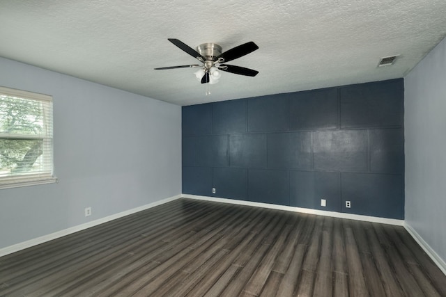 unfurnished room with a textured ceiling, dark wood-type flooring, a ceiling fan, visible vents, and baseboards