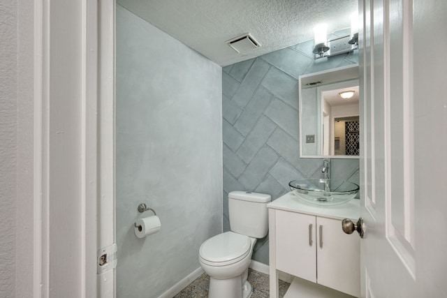 bathroom with visible vents, toilet, a textured ceiling, vanity, and tile walls