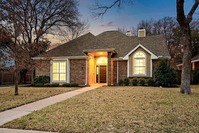 ranch-style home with a yard, brick siding, roof with shingles, and a chimney