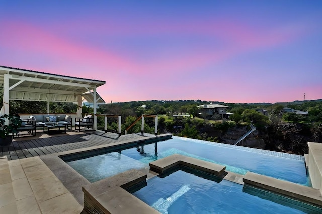 pool at dusk with a deck, a pool with connected hot tub, and an outdoor hangout area