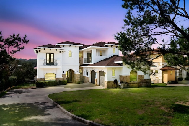 mediterranean / spanish home with stucco siding, stone siding, a lawn, and concrete driveway