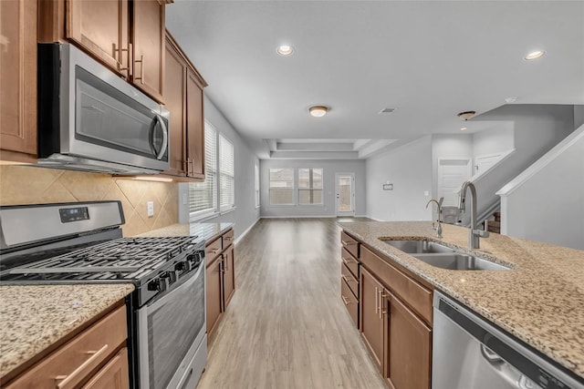 kitchen featuring appliances with stainless steel finishes, brown cabinetry, a sink, light stone countertops, and light wood-type flooring