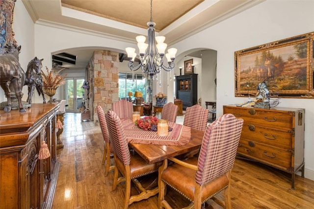 dining space with wood-type flooring, arched walkways, a raised ceiling, and a chandelier
