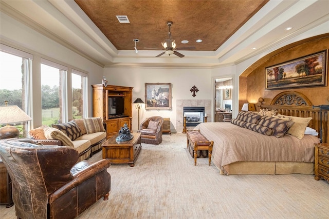 bedroom with a tile fireplace, carpet, ornamental molding, visible vents, and a tray ceiling