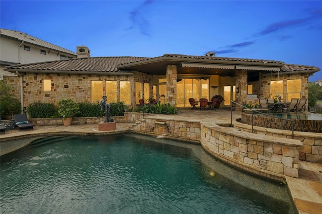 rear view of property with a patio, stone siding, an outdoor pool, a chimney, and a tiled roof