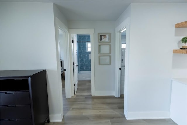 hallway featuring light wood finished floors and baseboards