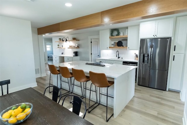 kitchen featuring white cabinets, light countertops, stainless steel refrigerator with ice dispenser, a center island, and open shelves