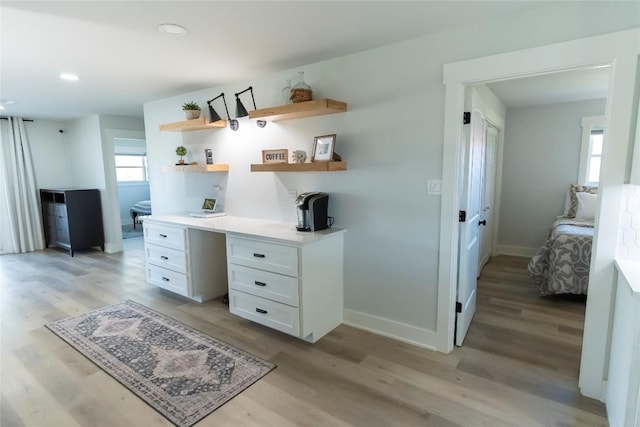 home office featuring light wood finished floors, recessed lighting, built in desk, and baseboards