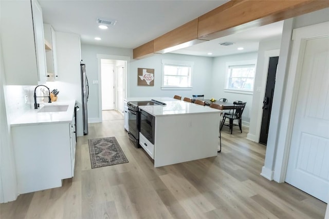 kitchen with visible vents, black range with electric stovetop, a sink, and white cabinetry