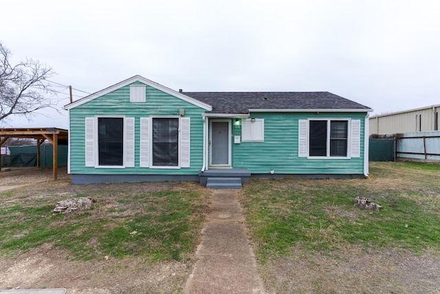 view of front of home featuring roof with shingles, fence, and a front lawn