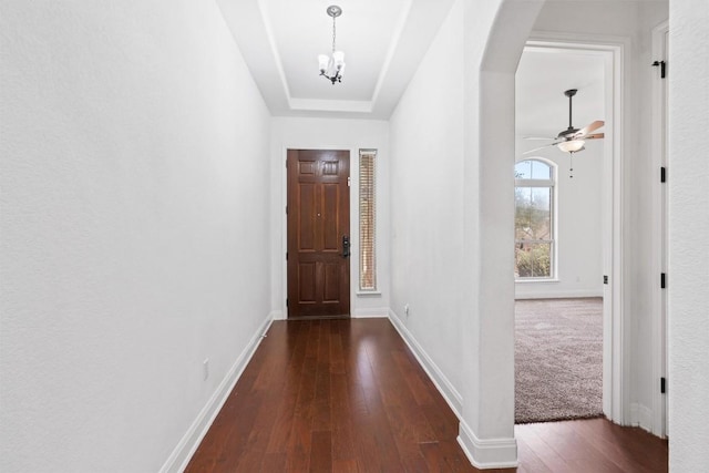 foyer with baseboards, arched walkways, dark wood-style flooring, and ceiling fan with notable chandelier