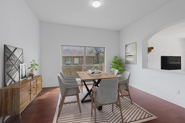 dining space with dark wood-type flooring, arched walkways, and baseboards