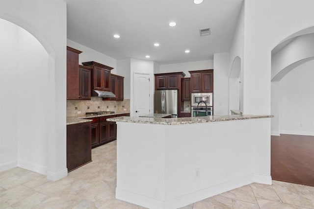 kitchen featuring a kitchen island with sink, stainless steel appliances, visible vents, decorative backsplash, and light stone countertops