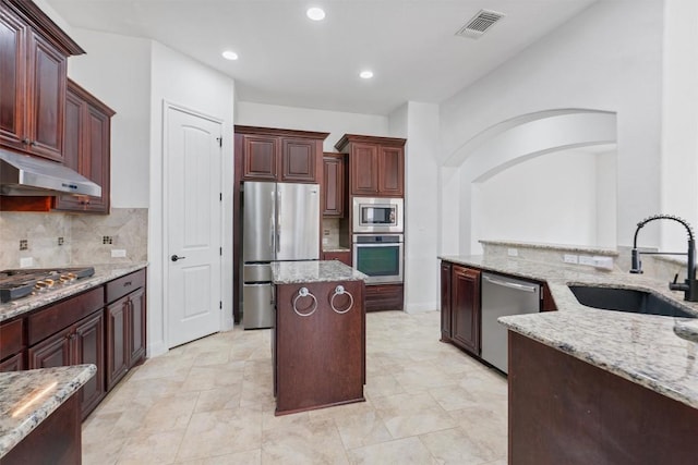 kitchen featuring under cabinet range hood, light stone counters, stainless steel appliances, and a sink