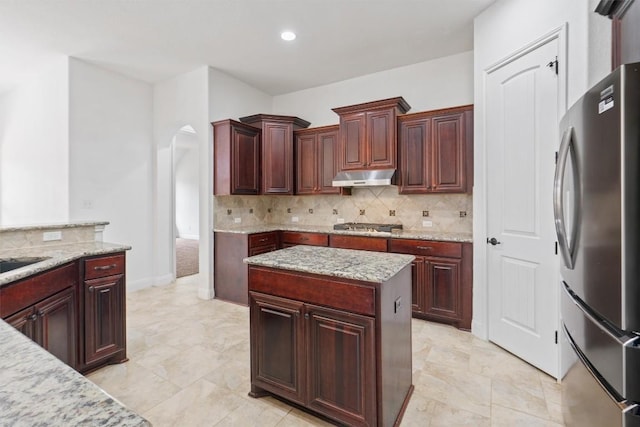 kitchen with light stone countertops, under cabinet range hood, tasteful backsplash, and stainless steel appliances