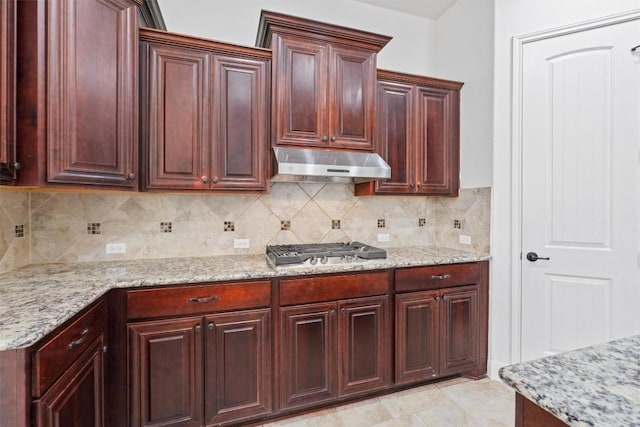 kitchen featuring stainless steel gas stovetop, backsplash, light stone countertops, and under cabinet range hood