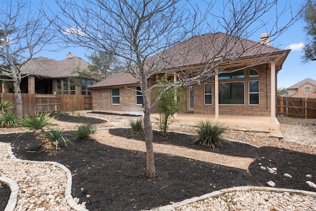 rear view of house with brick siding, a chimney, a patio area, and fence private yard