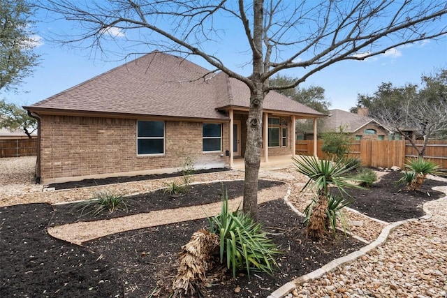 rear view of house featuring roof with shingles, fence, brick siding, and a patio