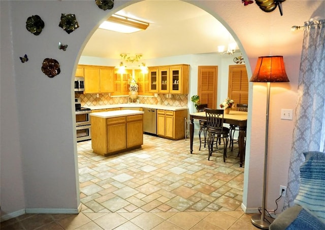 kitchen featuring arched walkways, light countertops, glass insert cabinets, appliances with stainless steel finishes, and a kitchen island