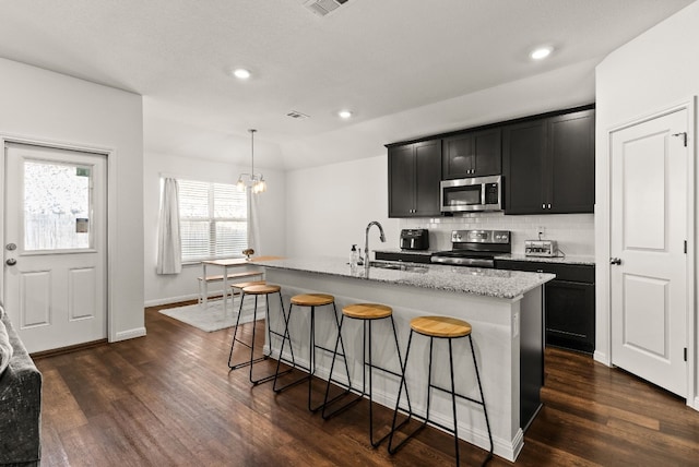 kitchen featuring appliances with stainless steel finishes, a sink, a center island with sink, and decorative light fixtures